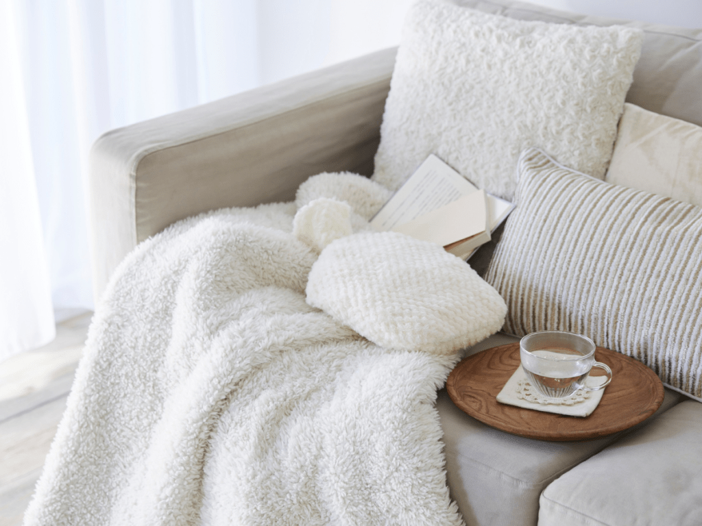 Comfortable sofa with soft blanket, book, and warm tea, representing everyday moments of calm and lifestyle well-being.
